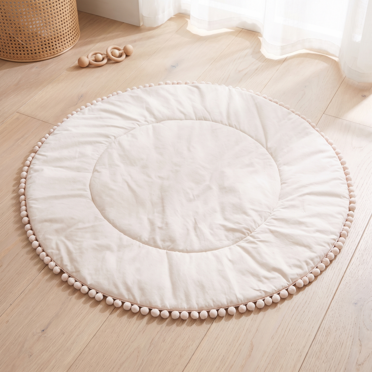 Round cream cotton pom pom baby play mat in a bright nursery