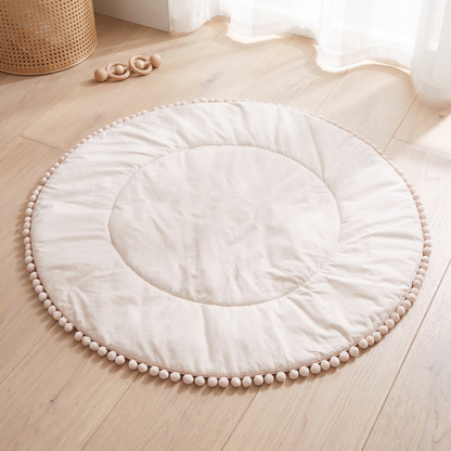 Round cream cotton pom pom baby play mat in a bright nursery