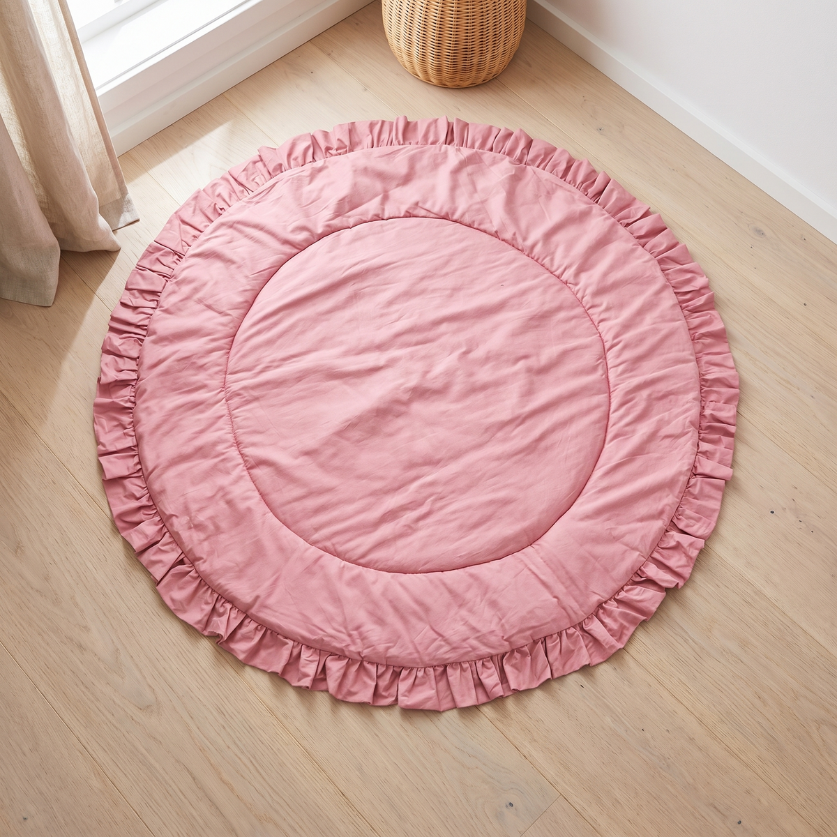 Round rose pink quilted cotton playmat with ruffle border on the floor of a bright nursery
