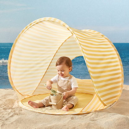 Toddler playing with sand bucket and shovel inside the yellow striped beach tent