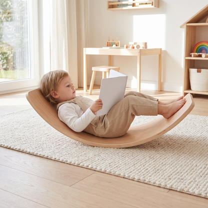 Toddler relaxing in the wooden balance board used as a rocker with a book