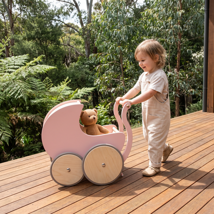 Child taking a teddy for a walk in the wooden doll pram on a sunny deck