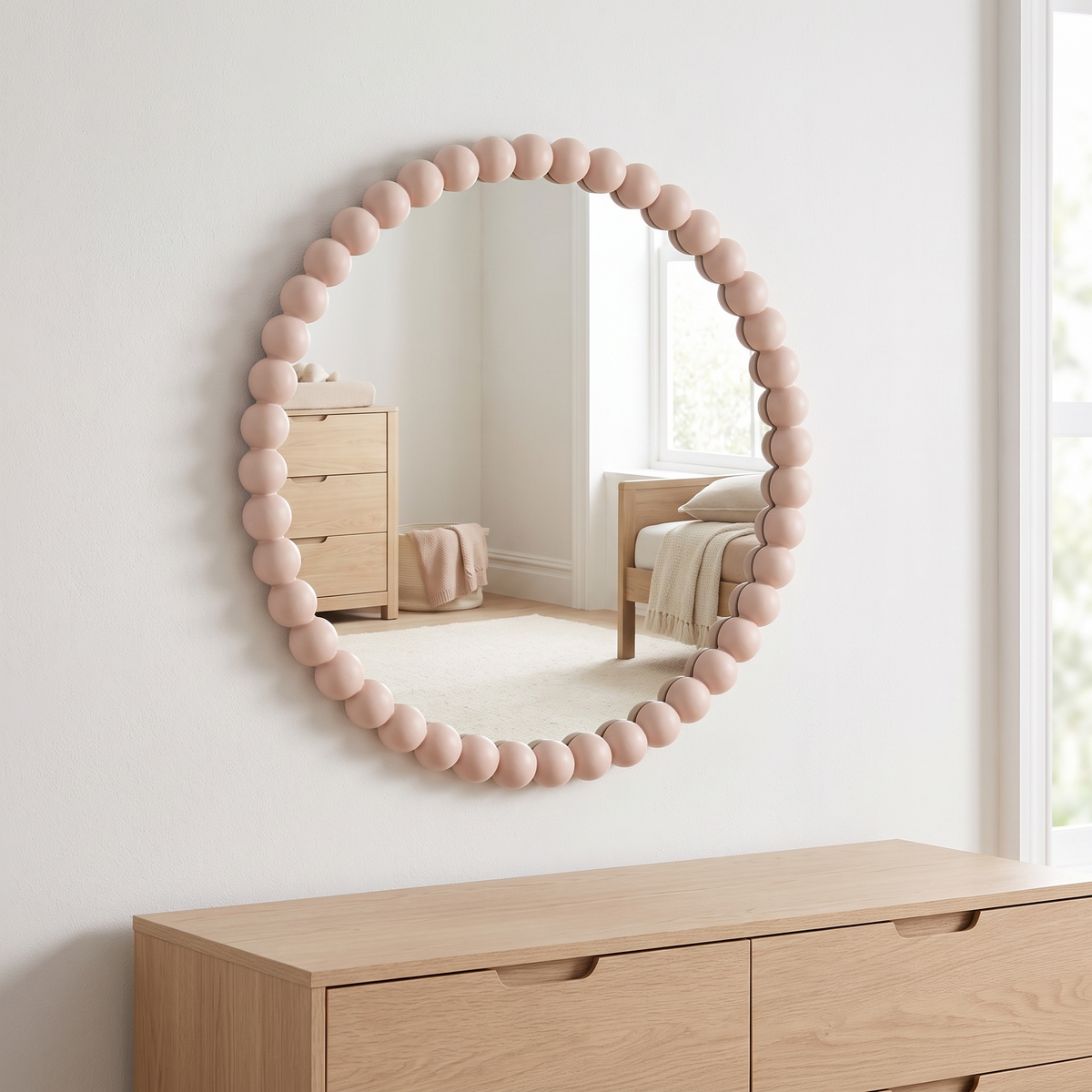 Round pink bobbin mirror above an oak dresser in a kids room