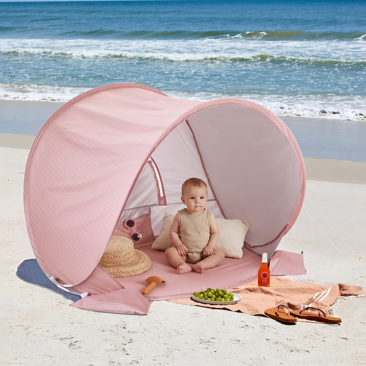 Baby sitting in the shade inside the striped beach tent with a pillow