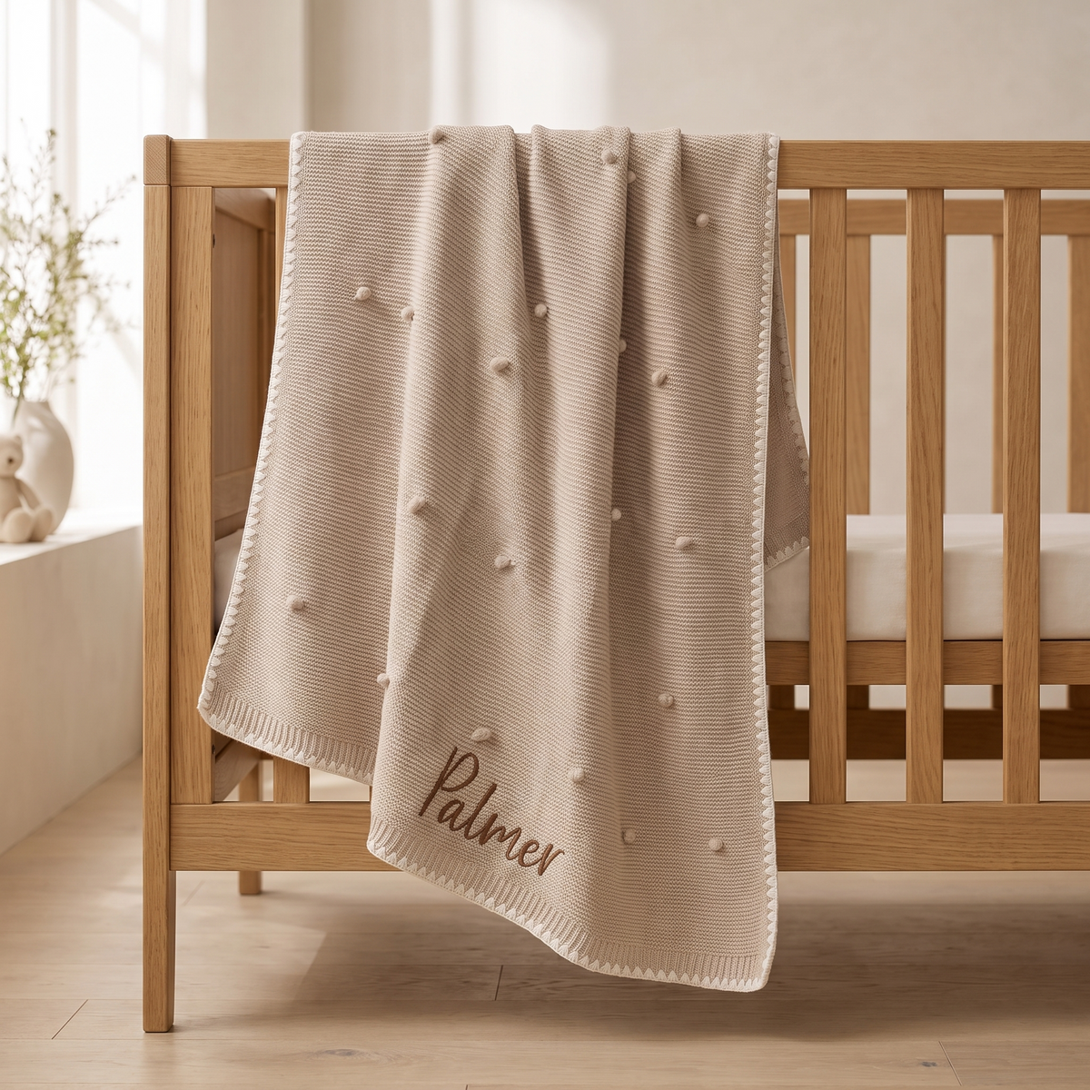Personalised cream bobble knitted baby blanket with embroidered name on a cot