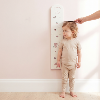 Woodland height chart mounted on a nursery wall beside a cot