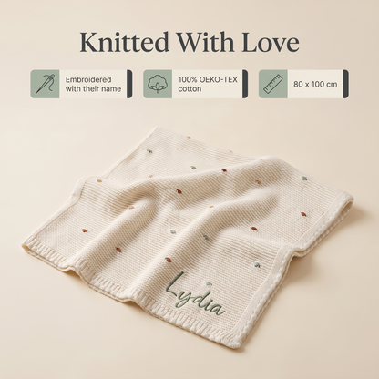 Baby lying on a personalised knitted bobble blanket with cream edging