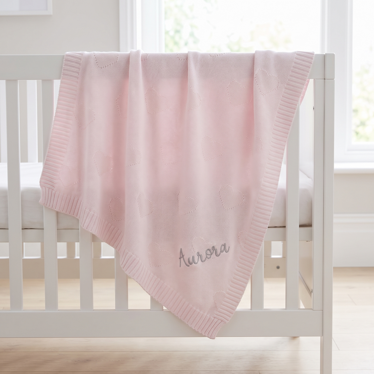 Personalised pale pink heart jacquard baby blanket with silver embroidered name on a cot