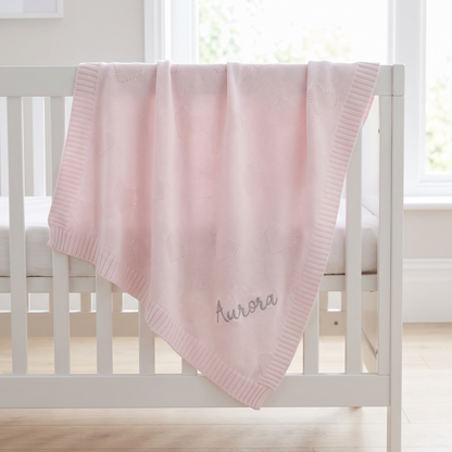 Personalised pale pink heart jacquard baby blanket with silver embroidered name on a cot