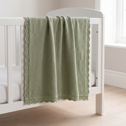 Sage green knitted cotton baby blanket folded on a nursery cot