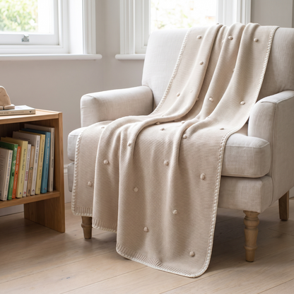 Cream bobble knit baby blanket draped over a cot in a soft neutral nursery