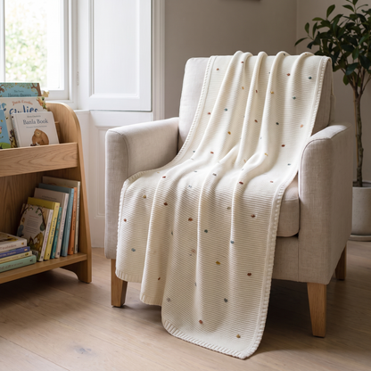 Multi-colour bobble knit baby blanket draped over a cot in a bright nursery