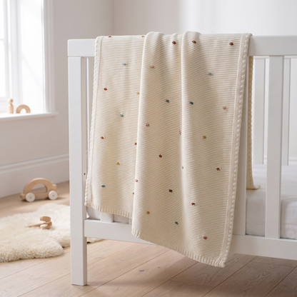 Multi-colour bobble knit cotton baby blanket folded in a nursery