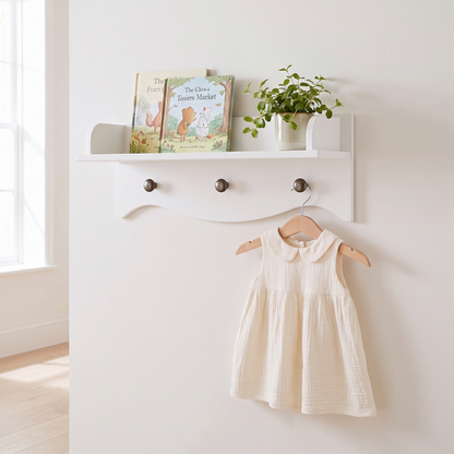 Little Teekie white nursery wall shelf with three hanging pegs styled with books and a robe
